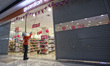 A shop assistant opens the rolling door of a cosmetic and healthcare store at a shopping m...