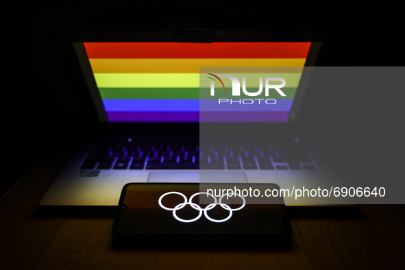 Olympic rings symbol is displayed on a mobile phone screen photographed with LGBT+ rainbow flag in the background afor the illustration phot...