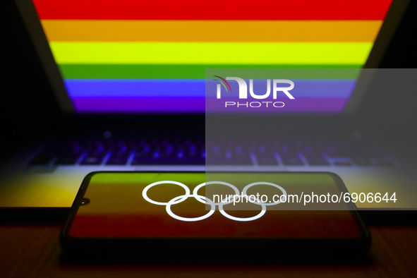 Olympic rings symbol is displayed on a mobile phone screen photographed with LGBT+ rainbow flag in the background afor the illustration phot...