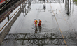 Long distance train passengers walk through the flooded railway tracks due to heavy rainfa...