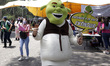 A person  wearing a Shrek motley   holds a placard to invite to be vaccinated against Covi...