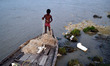 An indian boy sets up net on his boat before catching fishes on the polluted river bank of...