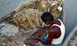 An indian fisher man sets up net on his boat before catching fishes on the  river bank of...