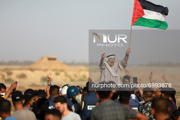 An elderly Palestinian man raises a national flag as youths shout slogans during a protest along the border fence, east of Khan Yunis in the...