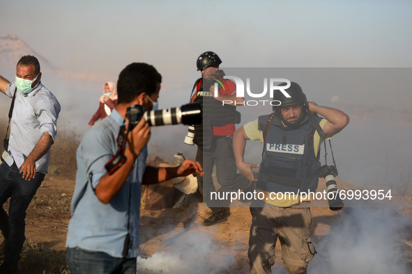 Palestinian photographers take cover from tear gas fired by Israeli security forces during a protest in the southern Gaza Strip August 25, 2...