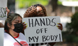 A woman holds a sign which reads, "Hands off my body!" as protestors wait for the march to...