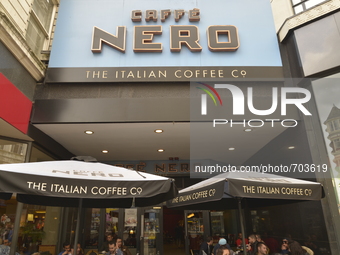 Light shining on to the Cafe Nero sign as people sit underneath parasols on Monday 11th May 2015 in Manchester. (