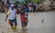 A mother holding her baby crosses a road covered in water and mud after another flash floo...