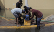 A group of people handle a liquid extraction device outside a flooded shopping centre in R...