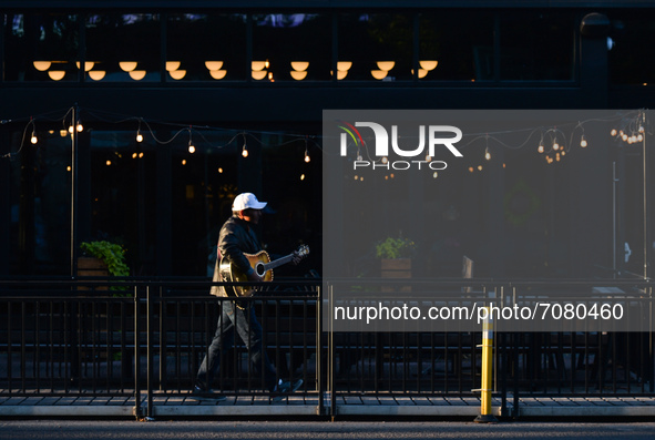 A man playing a guitar walks past empty tables outside a restaurant on Whyte Avenue in Edmonton center.
Alberta has declared a state of publ...