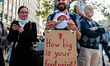 A man is holding his little born child and a placard in support of the planet, during the...