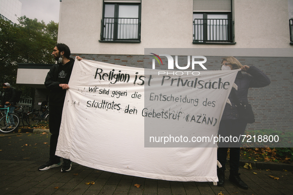 protesters hold banners " relion is private thing" during the protest over city decision allowing broadcasting the call for prayer at Cologn...