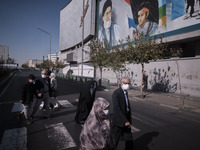 Iranian families wearing protective face masks walk under a portrait of Iran’s Supreme Leader Ayatollah Ali Khamenei as they walk along an a...
