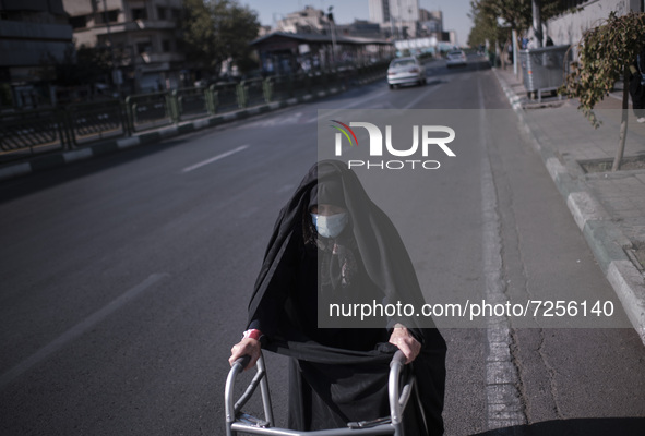 An Iranian elderly veiled woman wearing a protective face mask walks along an avenue with walker to the University of Tehran for taking part...