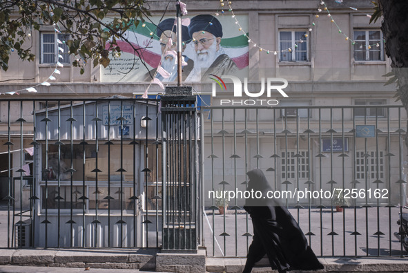 An Iranian veiled woman wearing a protective face mask walks past a portrait of Iran’s Supreme Leader Ayatollah Ali Khamenei as she arrives...