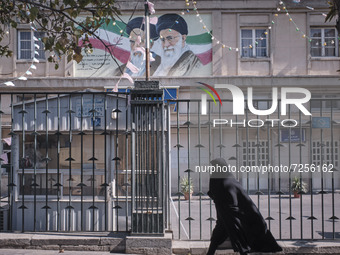 An Iranian veiled woman wearing a protective face mask walks past a portrait of Iran’s Supreme Leader Ayatollah Ali Khamenei as she arrives...