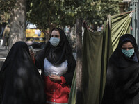 A female member of the Iranian Red Crescent (C) wearing a protective face mask checks body temperature of a veiled woman at an entrance of t...