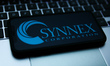 Synnex logo displayed on a phone screen and a laptop keyboard are seen in this illustratio...