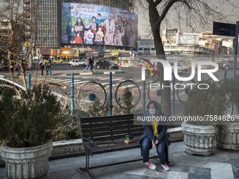 An Iranian woman wearing a protective face mask sits on a bench on a corner of a square in downtown Tehran on December 30, 2021, as a giant...