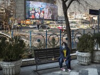 An Iranian woman wearing a protective face mask sits on a bench on a corner of a square in downtown Tehran on December 30, 2021, as a giant...