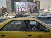 An Iranian yellow cab driver sits at his vehicle which is parked on a corner of a square in downtown Tehran on December 30, 2021, as a giant...