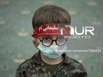 An Iranian young boy in military uniforms wearing a red headband with a Persian script that reads, I am Soleimani, as he takes part a death...