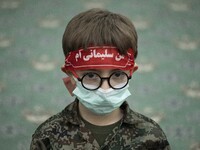 An Iranian young boy in military uniforms wearing a red headband with a Persian script that reads, I am Soleimani, as he takes part a death...