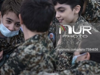 Iranian young boys in military uniforms talk to each other as one of them pastes a portrait of the Iranian top IRGC commander, General Qasem...