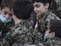 Iranian young boys in military uniforms talk to each other as one of them pastes a portrait of the Iranian top IRGC commander, General Qasem...