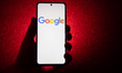 Google logotype on a smartphone held by a hand with a dark red background. Google closeup...