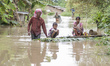 An Indian man wade through flood waters with his family on a raft as flash flood hit the r...