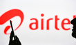 An image of a woman holding a cell phone in front of the Airtel logo displayed on a comput...