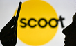 An image of a woman holding a cell phone in front of the Scoot Airline logo displayed on a...