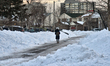 Woman walks along the road past mountains of snow in front of homes in Toronto, Ontario, C...