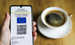 EU Digital COVID Certificate is displayed on a mobile phone screen photographed with a cup...