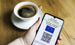 EU Digital COVID Certificate is displayed on a mobile phone screen photographed with a cup...