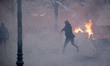 Demonstrator throws back to the police tear gas while a fire on a road barricade is burnin...