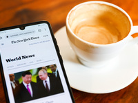 The New York Times website is displayed on a mobile phone screen photographed with a cup of coffee in the background for illustration photo...