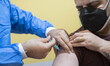 An Iranian man wearing a protective face mask receives a dose of the new coronavirus disea...