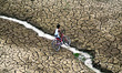 An indian youth croees a narrow drain with his bicycle over dried mud on the banks of the...