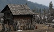 A woman carries a pitcher of water as she walks near a wooden residential house in Kupwara...