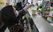 A woman wearing a protective face mask picks-up a food container loaded with an Iranian tr...
