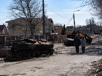 BUCHA, UKRAINE - APRIL 7, 2022 - A man and a woman walk along a street lined with destroyed military vehicles after the liberation of the ci...