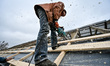 ZAPORIZHZHIA, UKRAINE - APRIL 16, 2022 - A worker saws a wood plank on the roof as a 70-ye...