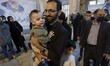 An Iranian man carrying his kid as he stands on a line to receive donated tea before visit...