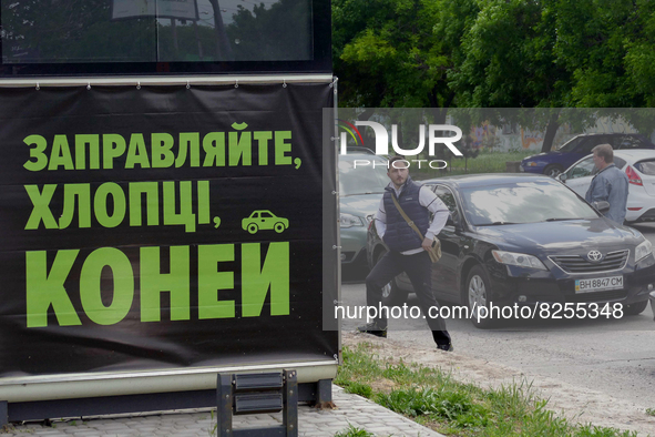 ODESA, UKRAINE - MAY 19, 2022 - A man steps on the pavement behind a banner in Ukrainian 'Refuel, Lads, Your Horses' as cars are stranded in...