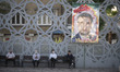 Iranian men sit next to a portrait of the Islamic Revolutionary Guard Corps' (IRGC) colone...