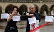 A barbed wired fence with sheets of paper reading 'Fear', 'Racism', 'pain' and 'Shame' wer...