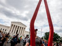 A man removes a large red coat hanger entitled "Gates of Hell" after the Supreme Court issued its opinion on Dobbs v. JWHO.  The opinion rev...