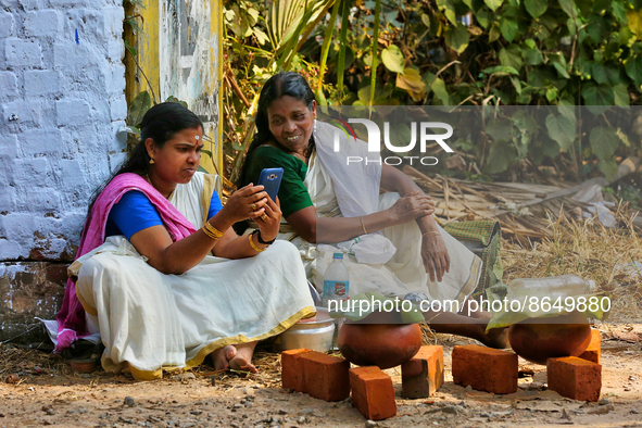 Hindu women look at a phone for updates from the Attukal Temple website as to when they can begin cooking pongala along the roadside on the...